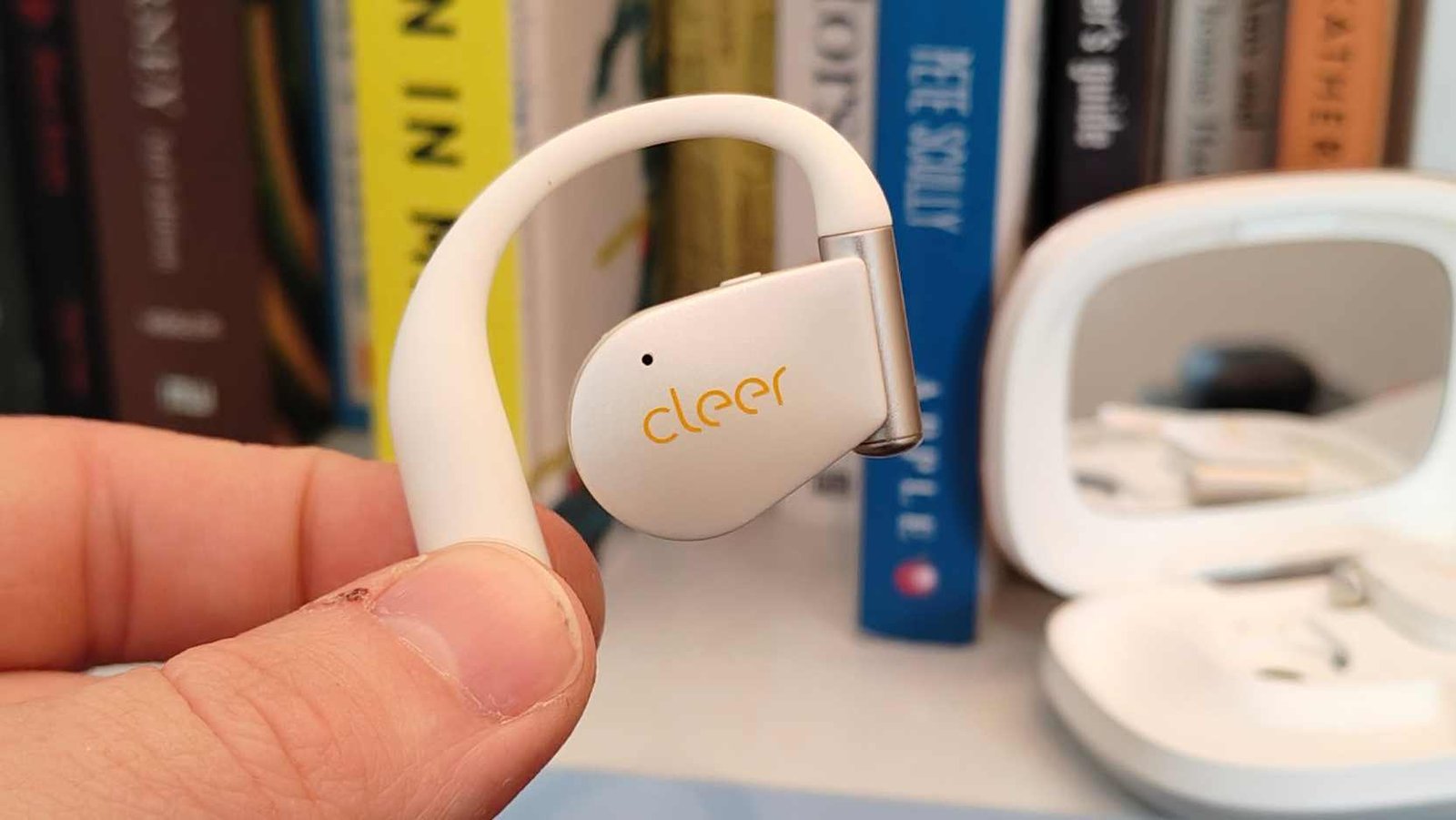 The Cleer Arc 5 bud being held in a man's hand, in front of some books.